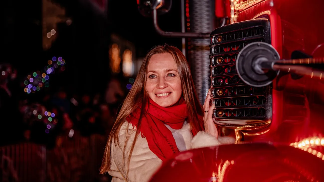 Smiling woman in a red scarf beside an illuminated truck at a night parade