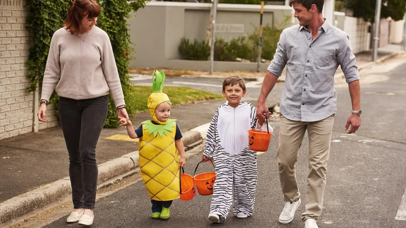 Parents walking children in Halloween costumes with treat buckets