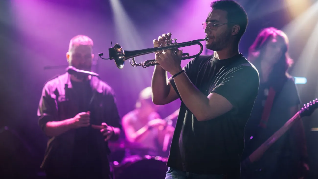 Trumpet player performing live on stage with band in purple light
