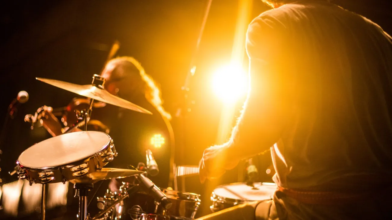 Drummer playing with a band under gold stage lights