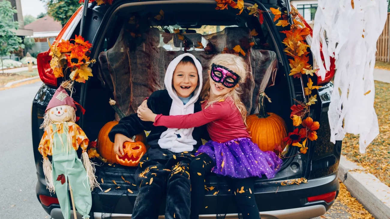 Trick or trunk. Children celebrating Halloween in trunk of car. Boy and girl with red pumpkins celebrating traditional O