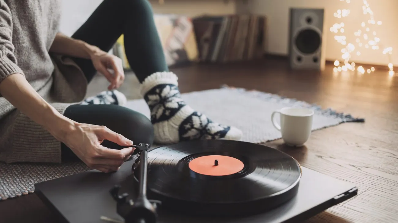 Young woman listening to music, relaxing, enjoying life at home. Girl wearing warm winter clothes having fun. Turntable 