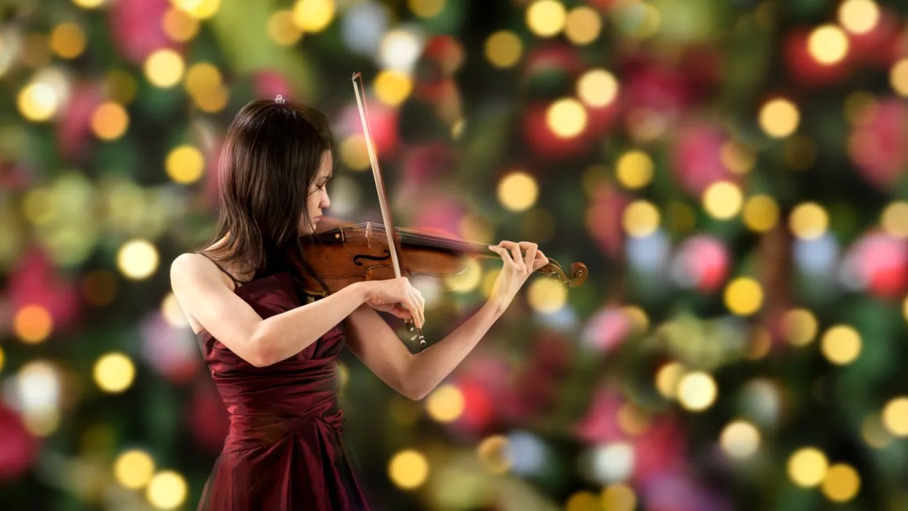 Young violinist playing beside a Christmas tree