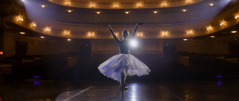 A ballerina in a white tutu dancing alone on a lit theater stage