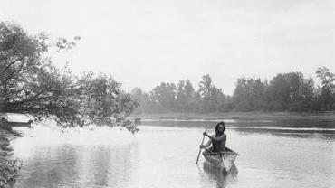 Native American man with canoe on river