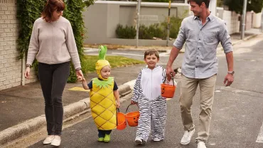 Parents walking children in Halloween costumes with treat buckets