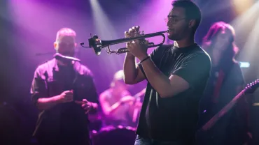 Trumpet player performing live on stage with band in purple light