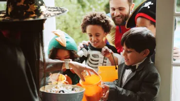 Children, woman and sweets at door on halloween for tradition, support and trick or treat. Holiday, neighborhood kids an