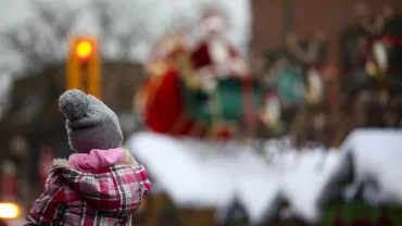 Girl on her father's shoulders watching Santa at a parade
