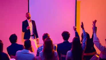 Speaker answering audience questions beside a screen