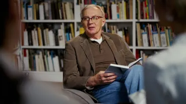 Man reading aloud from a book to a group