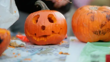 Hands carving Halloween pumpkins at a table
