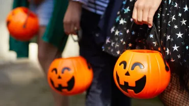 Children holding pumpkin candy bags while trick or treating