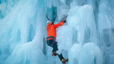 Alpinist man with ice climbing equipment on a frozen waterfall
