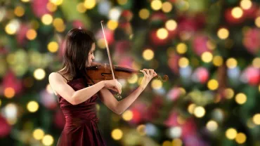 Young violinist playing beside a Christmas tree