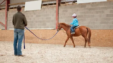 An instructor giving a young rider a lunging lesson in an indoor arena