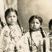Studio portrait of four unidentified young girls, possibly members of the Crow Indian tribe.