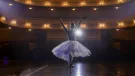 A ballerina in a white tutu dancing alone on a lit theater stage
