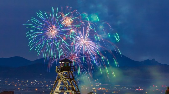 Fireworks bursting over a Montana town at dusk, with mountains behind